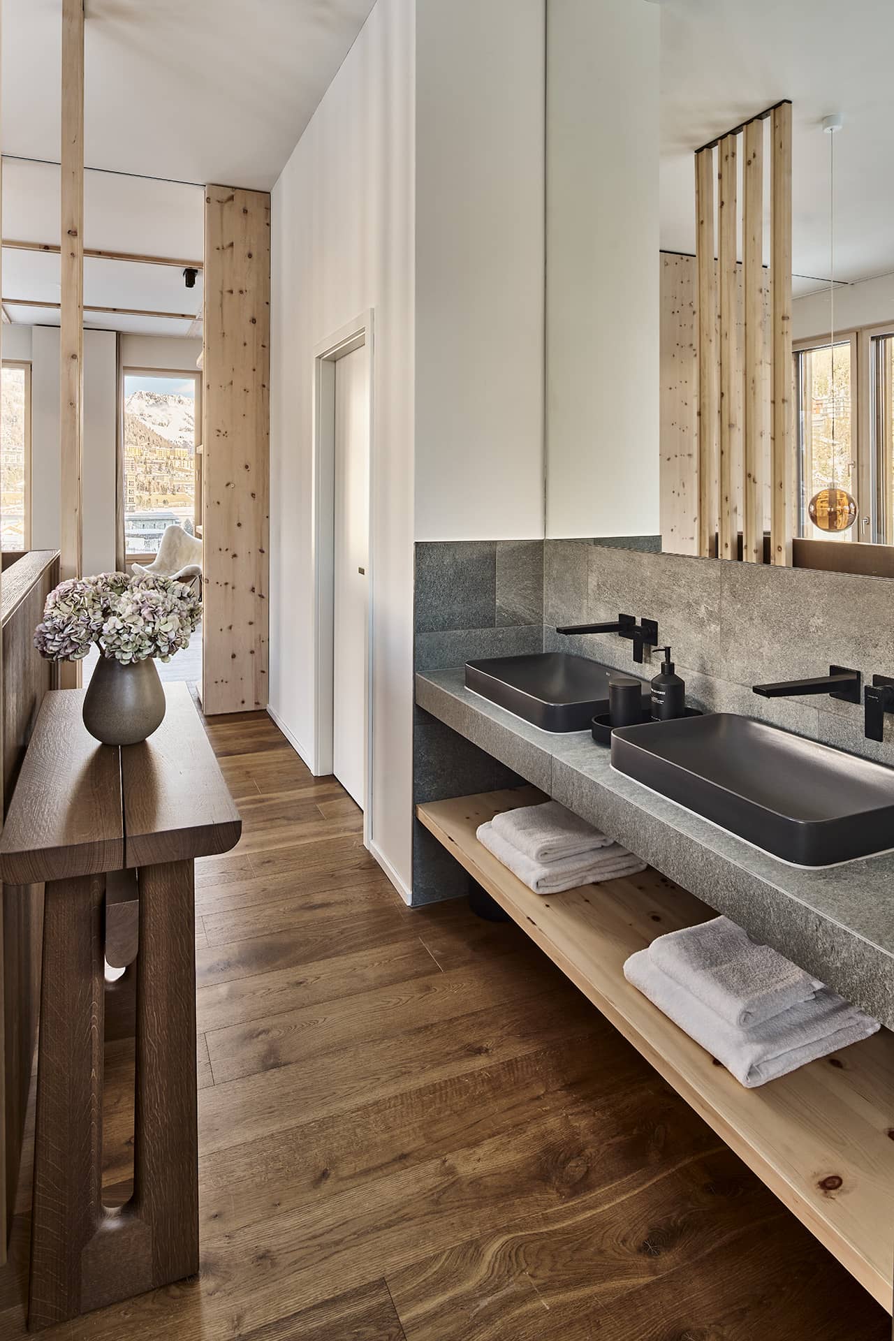 Offenes Badezimmer mit Doppelwaschtisch aus Stein, schwarzen Armaturen und Holzdetails.