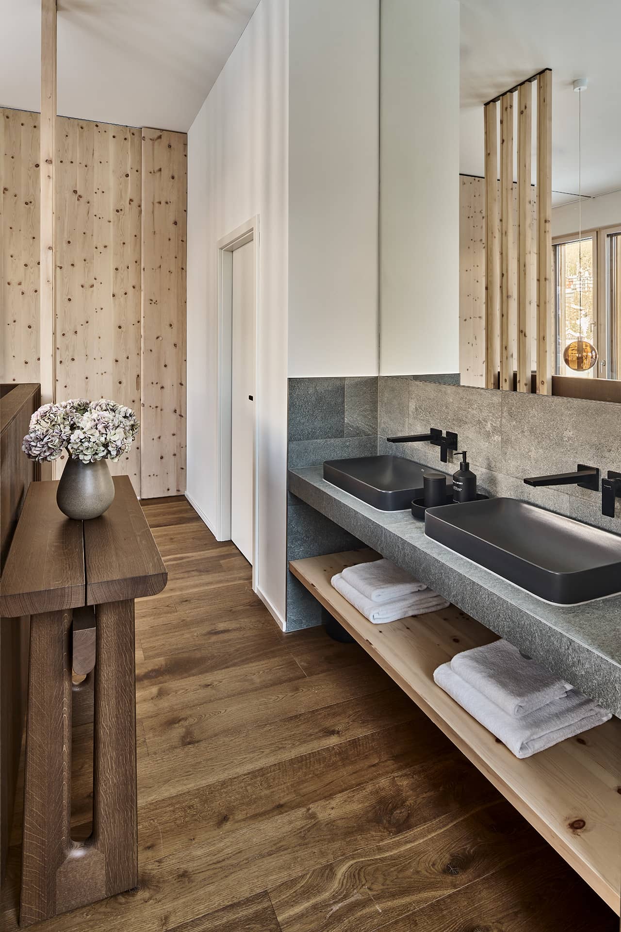 Modernes Badezimmer mit Doppelwaschbecken, Steinoberflächen und offenen Ablageflächen aus Holz.