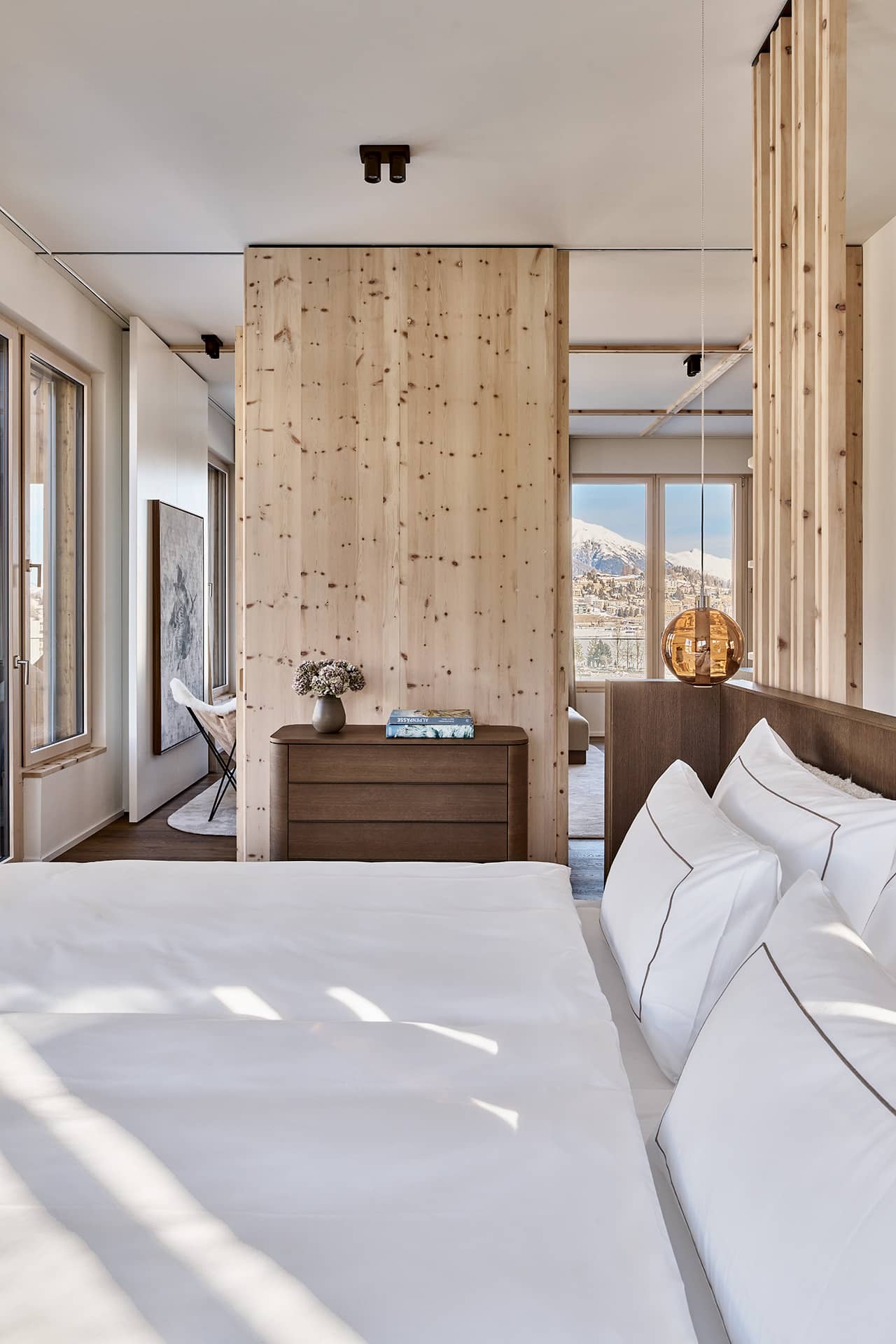Schlafzimmer des Masterpenthouses mit hochwertiger Bettwäsche, Arvenholz und Blick in den angrenzenden Wohnbereich