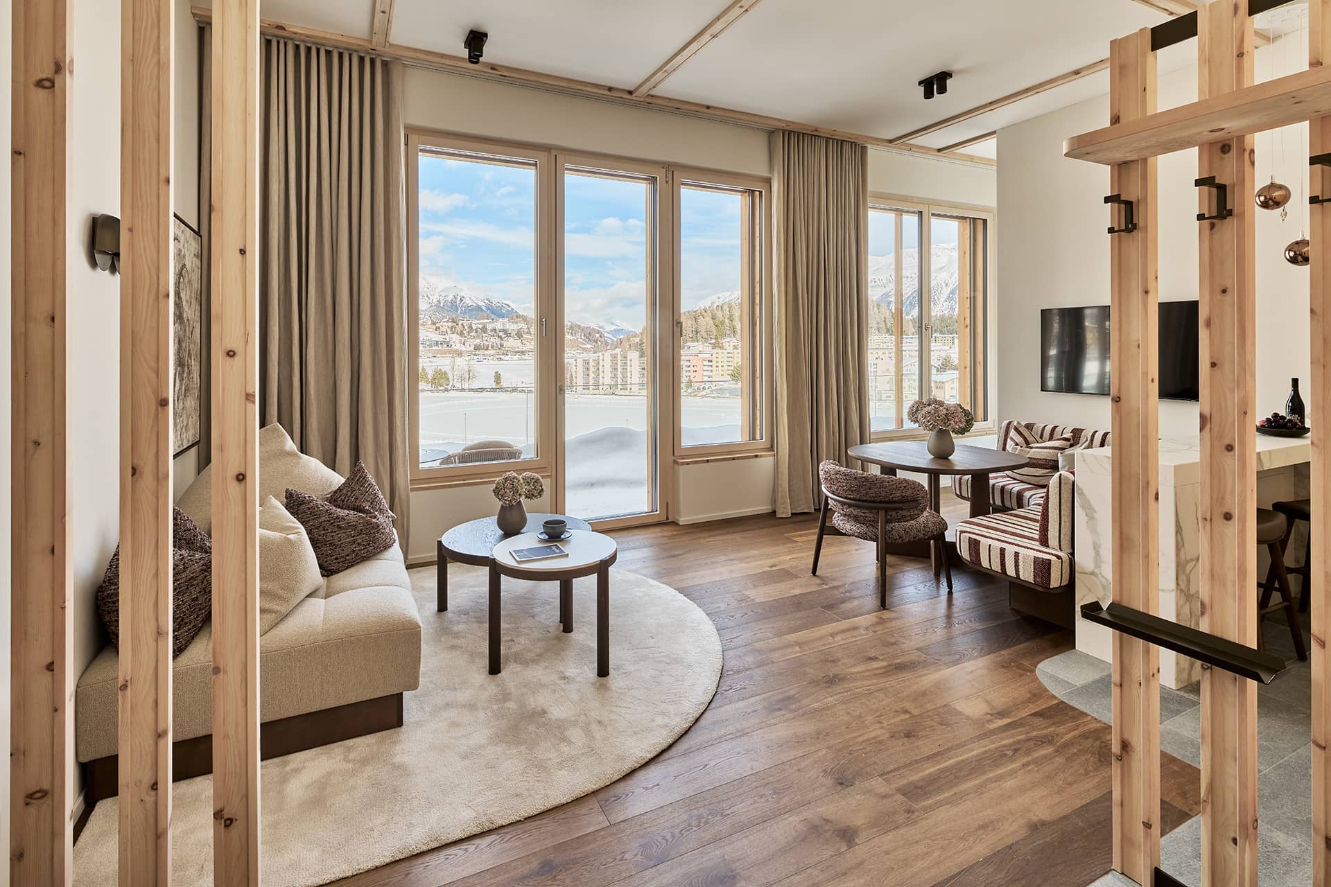 Heller Wohnbereich des Masterpenthouses mit gemütlicher Sitzecke, großen Fenstern und Blick auf die Engadiner Berge