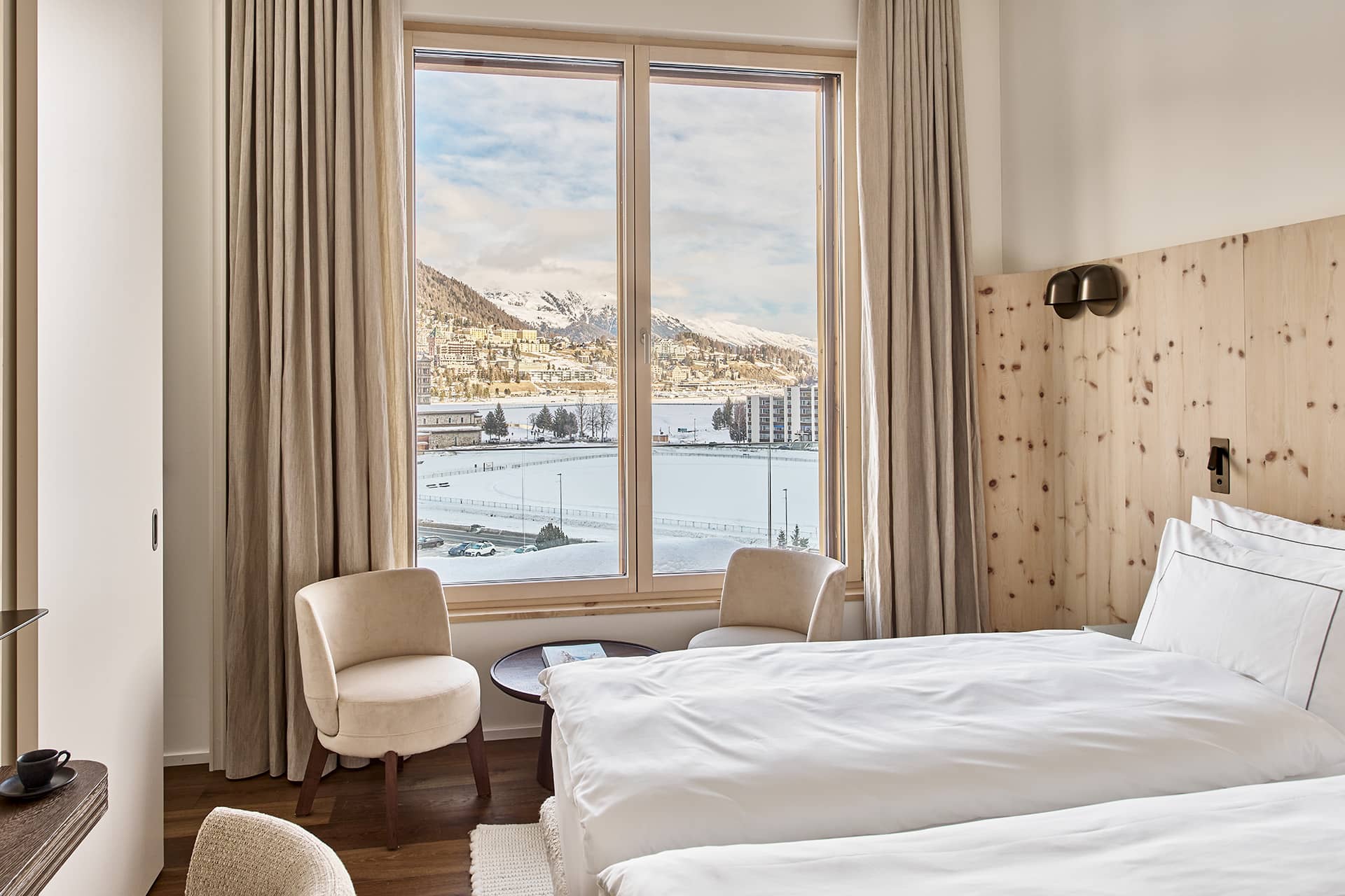 Helles Schlafzimmer im Masterpenthouse mit großen Fenstern und Blick auf St. Moritz und die verschneiten Berge