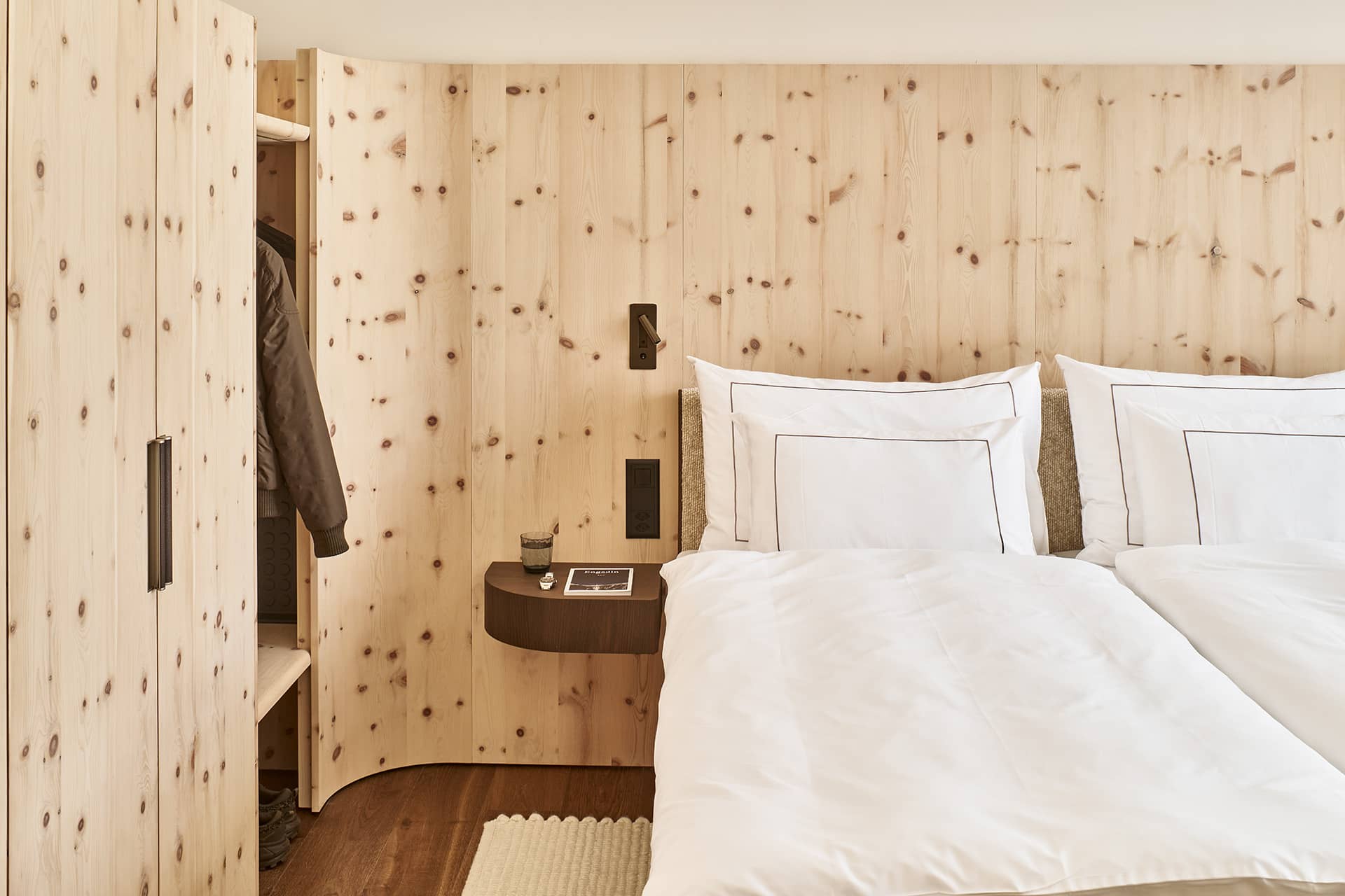 Schlafzimmer im Masterpenthouse mit Wandverkleidung aus hellem Arvenholz und hochwertiger weißer Bettwäsche