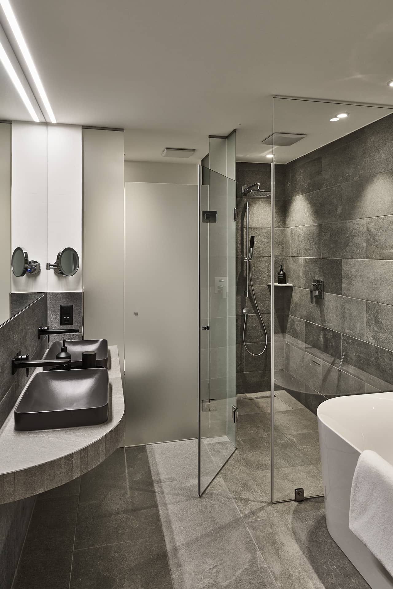 Modernes Badezimmer des Masterpenthouses mit Naturstein, Doppelwaschtisch, Glasdusche und freistehender Badewanne