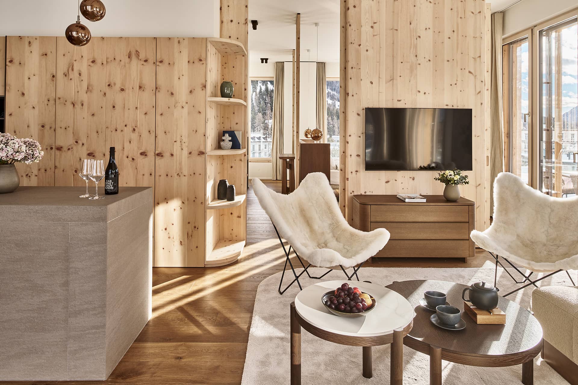 Wohnbereich mit Holzverkleidung, Sesseln, Fernseher und offener Küchenzeile.