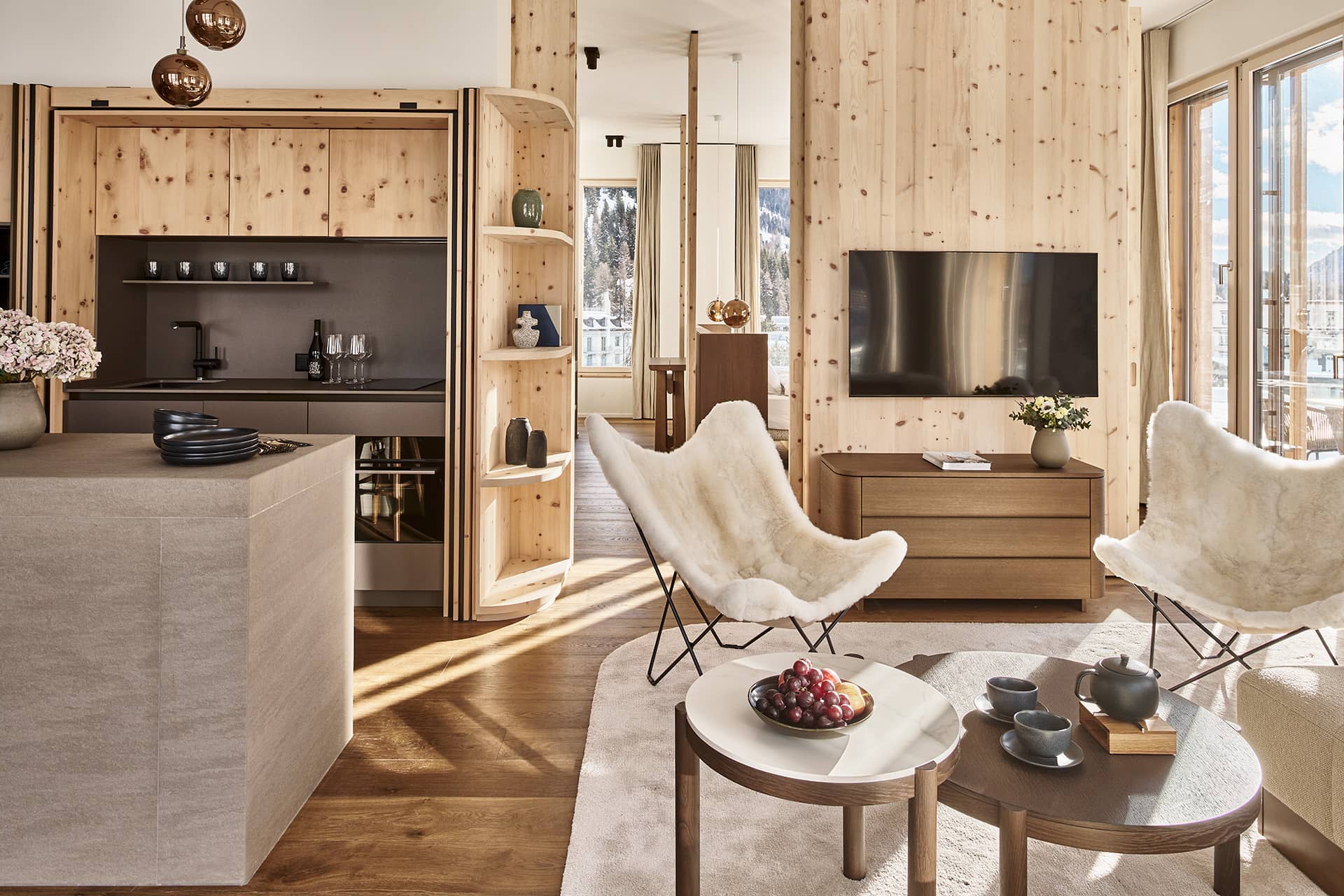 Wohnbereich mit Holzverkleidung, Sesseln, Fernseher und geöffneter Küchenzeile.
