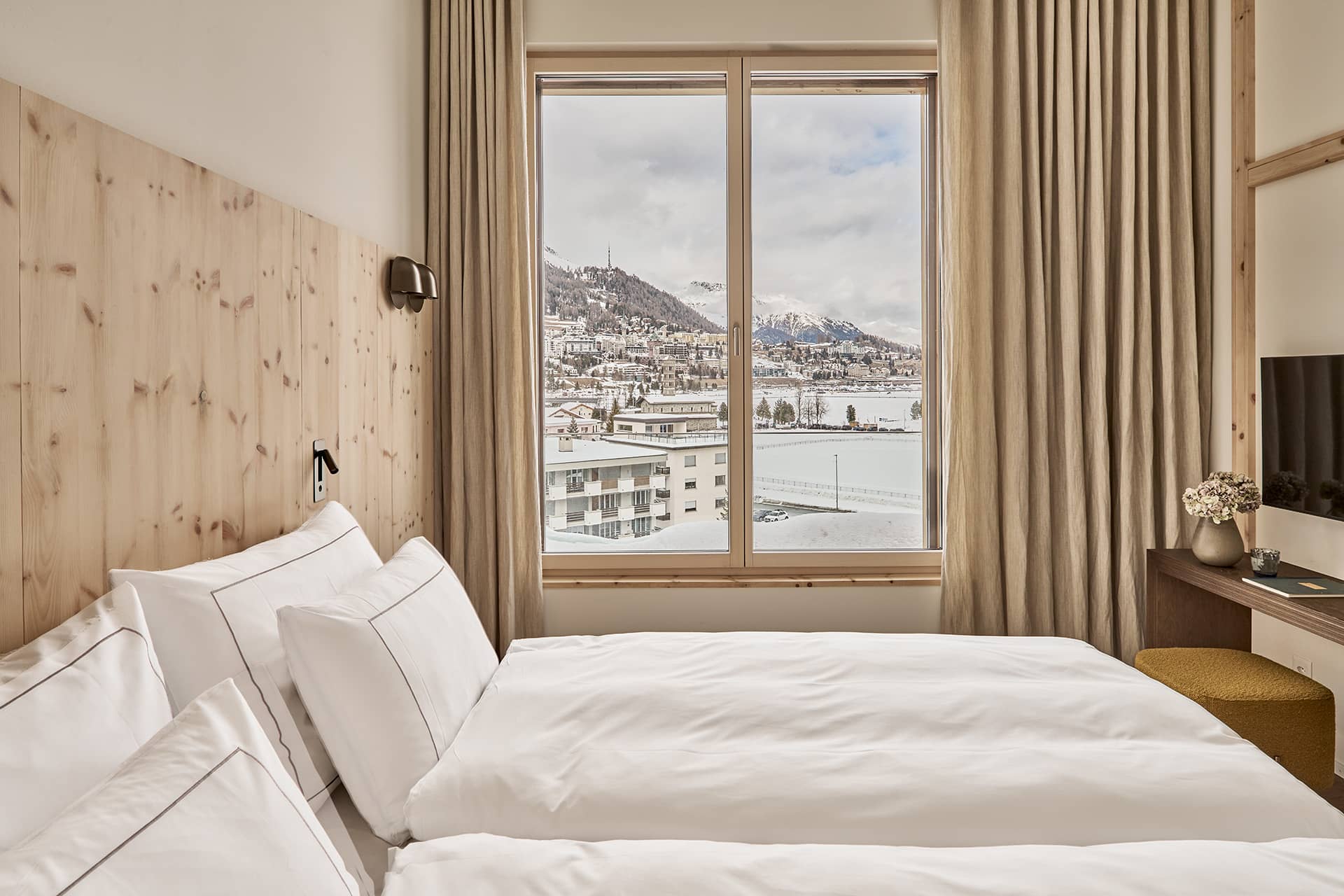 Schlafzimmer mit Doppelbett und grossem Fenster mit Blick auf St. Moritz und die Alpen.