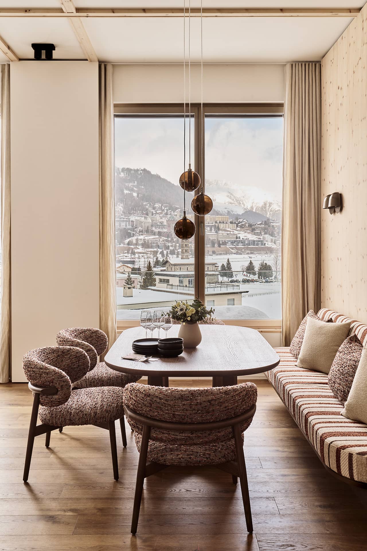 Essbereich mit Polsterbank, Esstisch und grossem Fenster mit Blick auf St. Moritz.