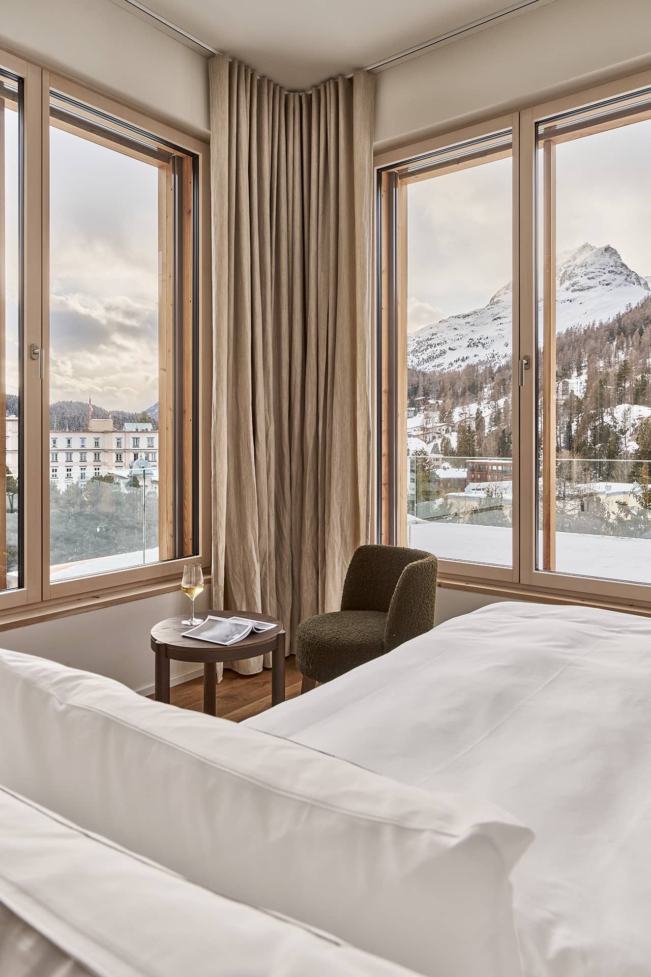 Schlafzimmer mit Doppelbett und Eckfenstern mit Blick auf die verschneite Berglandschaft.